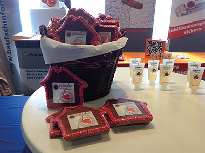 Ein Korb voller hausförmiger Lebkuchen auf einem Stehtisch vor einem Messestand.